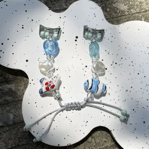 Detail of handcrafted beaded watch band with ceramic fish charm and blue heart beads