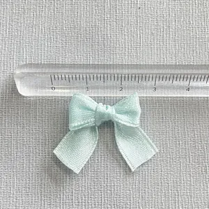 Detail of light blue satin ribbon bow with ruler showing 3cm width for DIY crafts