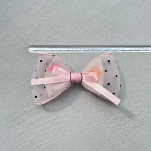 Macro view of pink polka dot mesh bow hair clip with satin layers and measurement ruler