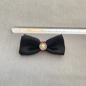 Close-up of a 6cm black satin bow with red band, faux pearl and rhinestone detail