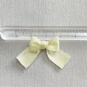 Top view of a 3.2cm cream satin bow accessory measured with a transparent ruler