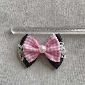 Detalle de un lazo para el pelo con cuadros rosas y satén negro con encaje y perla