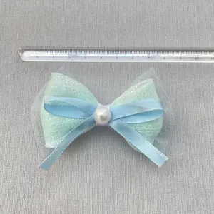 Detail van blauwe satijnen strik met parel en tule, toont breedte van 8,5cm op liniaal