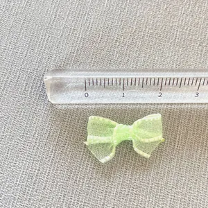 Detail of light green mesh bow with white stitching and ruler for size scale reference
