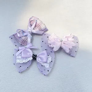 Detailed view of three purple handmade bow hair clips with pearls and lace on gray fabric