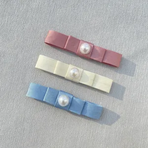 Detail of satin bow hair clips with pearls in pink, beige and light blue colors