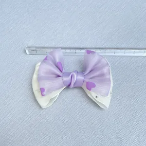 Purple satin bow with heart patterns and rhinestones shown on a measuring ruler