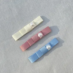 Close-up of three satin bow hair clips with pearls in cream, pink, and blue colors
