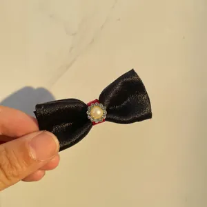 Detail of a handmade black satin bow hair clip with a center faux pearl and rhinestones