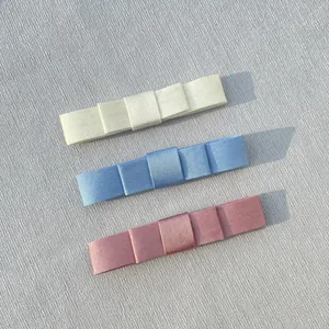 Three satin ribbon bow hair clips in cream, blue and pink shown from a top-down view