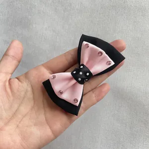 Detalle de un lazo para el pelo en satén rosa y negro con cinta de lunares y brillantes rosas