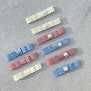 Detail of multi-colored satin bow hair clips with pearls on a textured gray fabric
