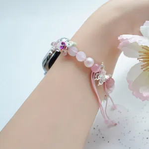 Detail of pink crystal beaded iWatch strap with butterfly and flower charms on wrist
