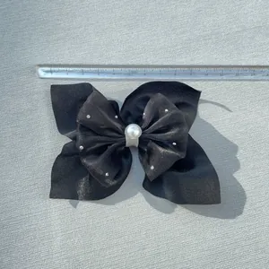Detail of a black bow hair accessory with a white pearl, rhinestones and a scale ruler