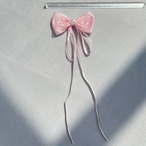 Pink satin bow hair accessory with white polka dot mesh and a pearl center on fabric