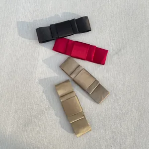 Flat lay of stacked satin bow hair clips in black, burgundy, and champagne gold colors