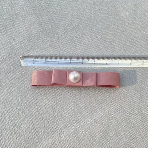 Pink satin ribbon bow with pearl center measuring 8.5cm on a transparent ruler