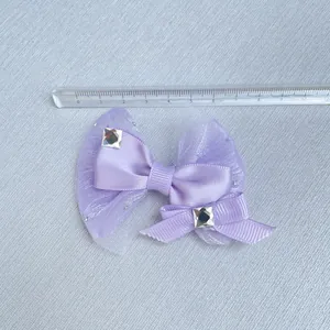 Detail of purple satin and glitter mesh bows with rhinestones next to a scale ruler