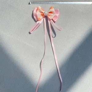 Macro detail of a pink layered satin bow hair accessory with pearls and size measurement