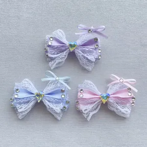 Dettaglio di tre fermagli a fiocco in pizzo con gemme a cuore in viola rosa e azzurro