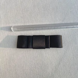 Top view of a 9.5cm black satin bow accessory measured with a ruler on a textured surface