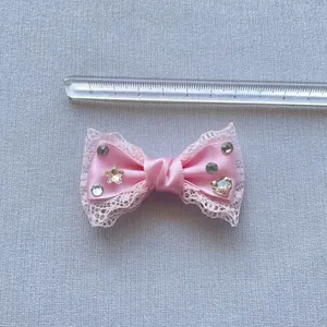 Vista dettagliata di un fiocco in pizzo rosa da 6cm con strass per capelli e decori