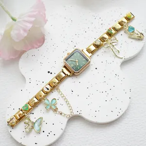 Détail d'une montre carrée dorée avec cadran vert et bracelet à breloques de style italien