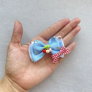 Blauwe haarstrik met kersen hanger en strass steentjes gepresenteerd op een hand