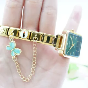 Détail d'une montre à quartz dorée avec cadran vert et charms sur bracelet modulable