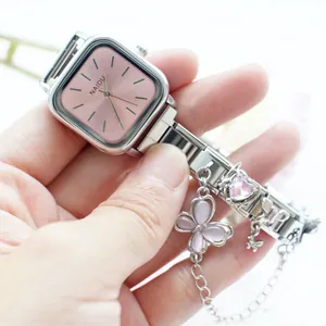 Détail de montre carrée argentée pour femme avec cadran rose et breloques papillon