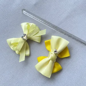 Dettagli di due fiocchi per capelli in raso giallo con cristallo a forma di cuore