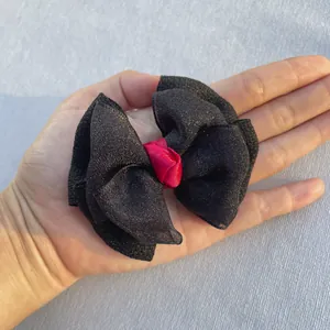 Détail d'un nœud papillon en tulle noir avec centre en satin rouge tenu en main