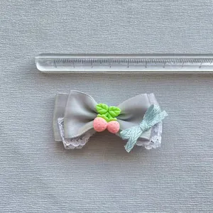 Detail einer grauen Satinschleife mit weißem Spitzenbesatz und rosa Fruchtanhänger