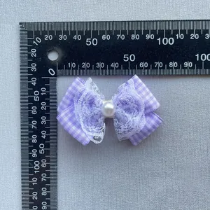 Purple plaid fabric bow with white lace trim and center pearl, measured on a scale