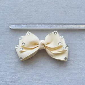 Detailed view of cream bow accessory with rhinestones next to a measuring ruler