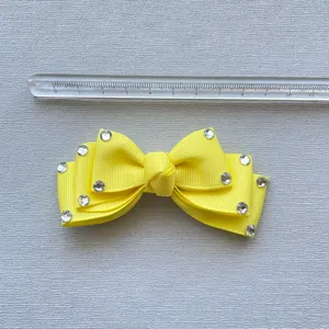 Macro detail of yellow ribbon bow accessory with rhinestones shown against a metric ruler