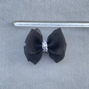 Detail view of a 9cm handmade black fabric bow with polka dot center and size ruler