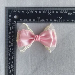 Nœud en satin rose avec bordure en dentelle blanche pour cheveux, présenté avec une règle