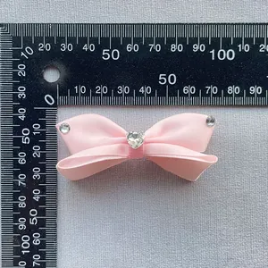 Dettaglio fiocco in raso rosa con strass a cuore su sfondo con righello graduato