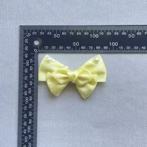 Close-up of a light yellow satin bow accessory with white pearls and measuring scale