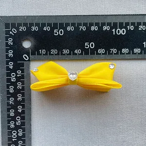 Dettaglio del fermaglio a fiocco in raso giallo con strass a cuore di misura 6,5 cm