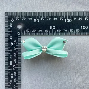 Dettaglio di un fiocco in nastro verde menta da 5cm con strass a cuore e righello di misurazione