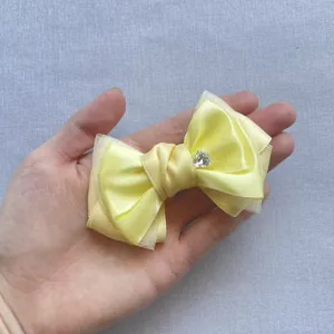 Close-up of a handmade yellow satin bow with mesh layers and a heart-shaped rhinestone