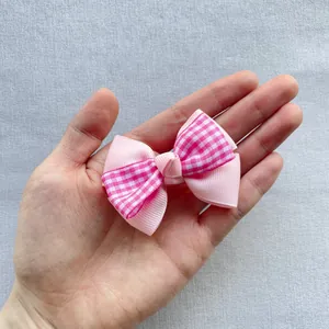 Pink ribbed and checkered ribbon bow held in palm to show miniature size and texture