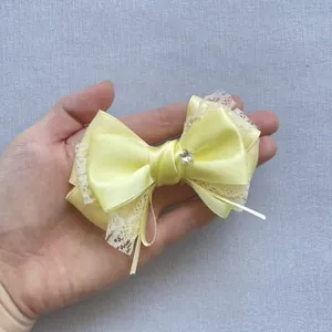 Detail of yellow satin bow with white lace trim and a star rhinestone center in hand