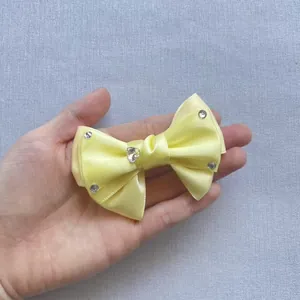 Close-up of yellow satin bow with heart rhinestone being held for size reference
