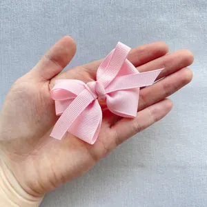 Pink grosgrain ribbon bow accessory held in hand showing texture and small size