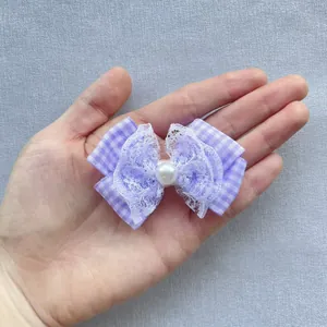 Detail of purple plaid bow hair clip with lace trim and pearl bead held in hand
