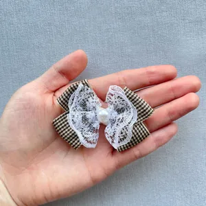 Close-up of handmade plaid bow with lace and pearl detail held in palm for size