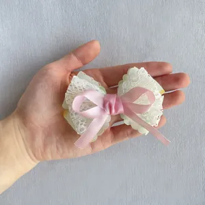 Détail d'un nœud en satin rose et dentelle tenu à la main pour l'échelle et texture
